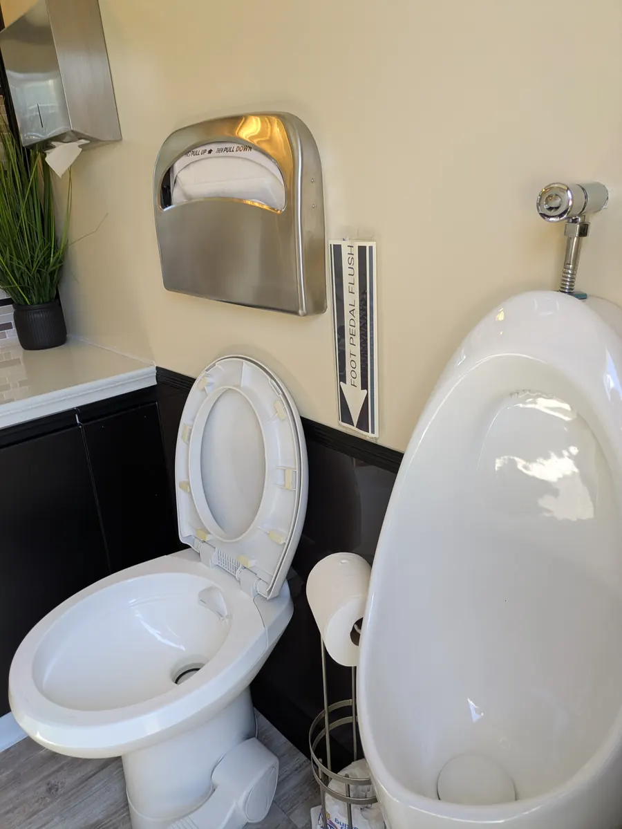 Private stall with flushing toilet, urinal, and seat-cover dispenser